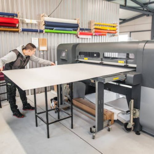 Technician worker operator works on large premium industrial printer and plotter machine in digital printshop office